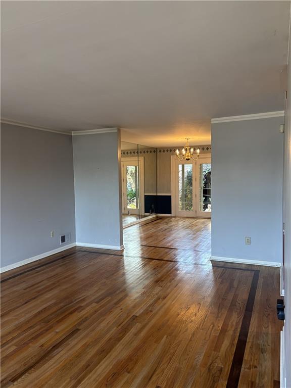unfurnished living room with baseboards, visible vents, ornamental molding, and a notable chandelier