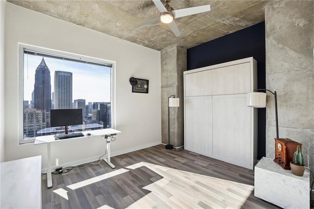 office space with wood-type flooring, a wood stove, and ceiling fan