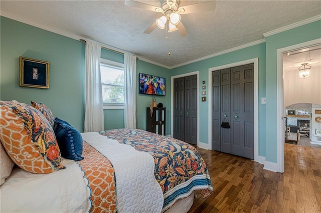 bedroom with a textured ceiling, wood finished floors, multiple closets, ornamental molding, and baseboards