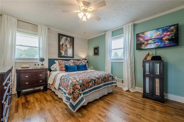 bedroom with wood finished floors, multiple windows, a textured ceiling, baseboards, and crown molding