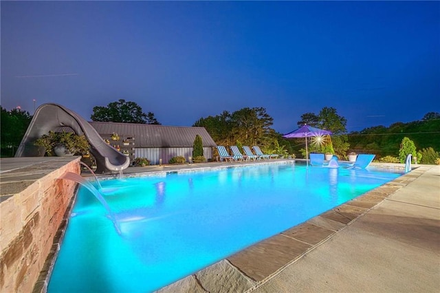 pool at twilight featuring a water slide and a patio area