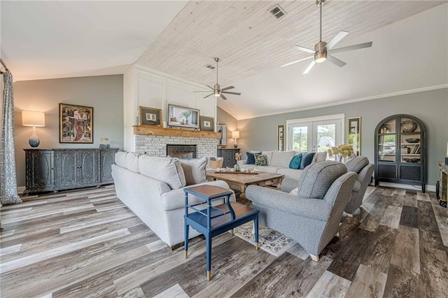 living area featuring lofted ceiling, ceiling fan, wood finished floors, a brick fireplace, and baseboards