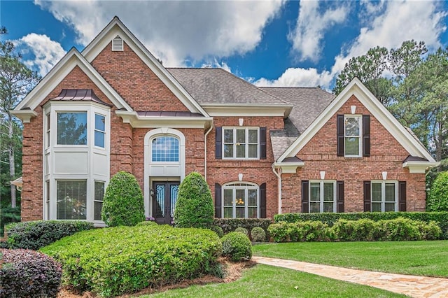 view of front of home with a front yard, brick siding, and roof with shingles