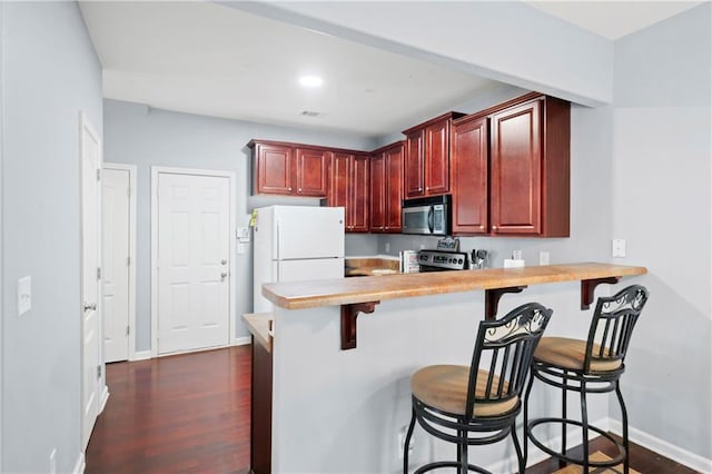 kitchen with a breakfast bar area, appliances with stainless steel finishes, kitchen peninsula, and dark hardwood / wood-style floors