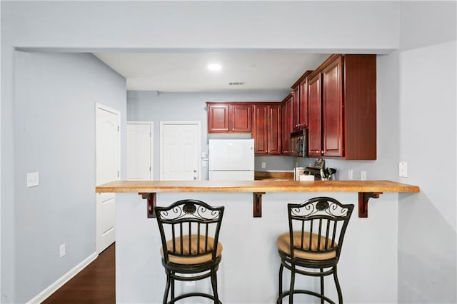 kitchen with dark wood-type flooring, stainless steel appliances, a breakfast bar, and kitchen peninsula