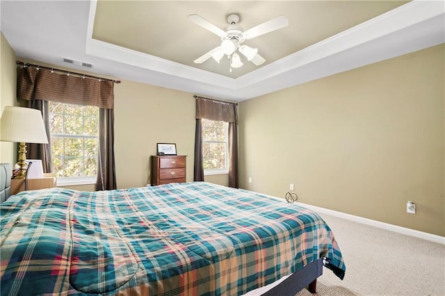 carpeted bedroom featuring multiple windows, a tray ceiling, and ceiling fan