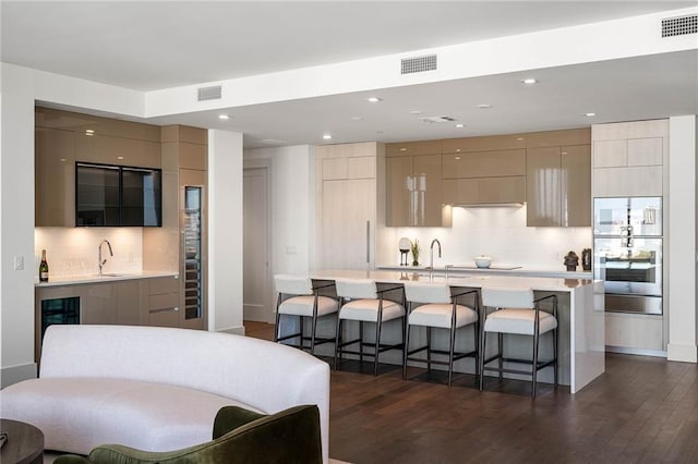 kitchen featuring backsplash, a center island with sink, wine cooler, dark hardwood / wood-style flooring, and a breakfast bar area