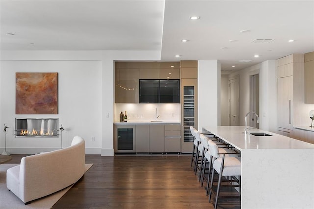 kitchen with a breakfast bar, dark wood-type flooring, a large island with sink, sink, and wine cooler