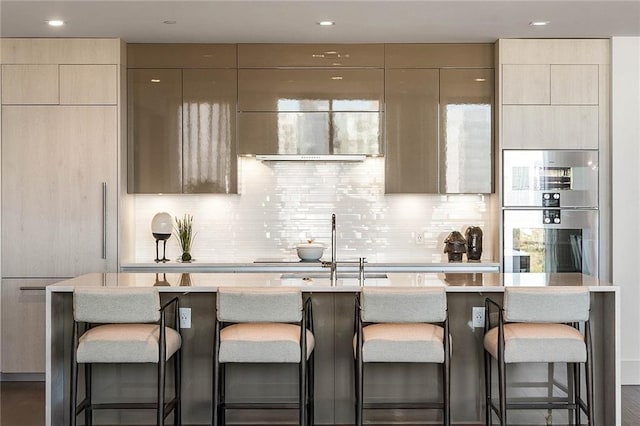 kitchen featuring decorative backsplash, a breakfast bar, an island with sink, and plenty of natural light