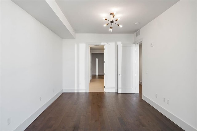 empty room with dark hardwood / wood-style flooring and a chandelier