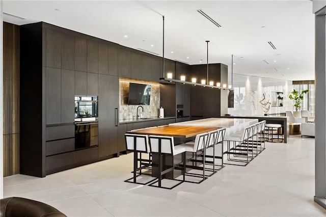 kitchen featuring wood counters, sink, decorative light fixtures, light tile patterned flooring, and a breakfast bar area