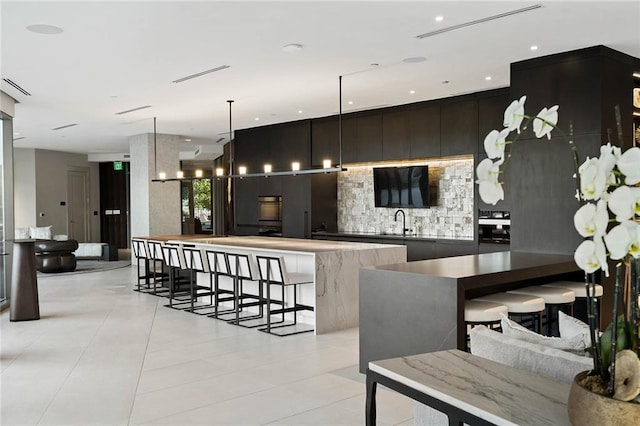 kitchen featuring a center island, sink, hanging light fixtures, light tile patterned flooring, and a breakfast bar area