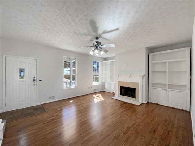 unfurnished living room featuring wood finished floors, built in shelves, a fireplace, and a textured ceiling