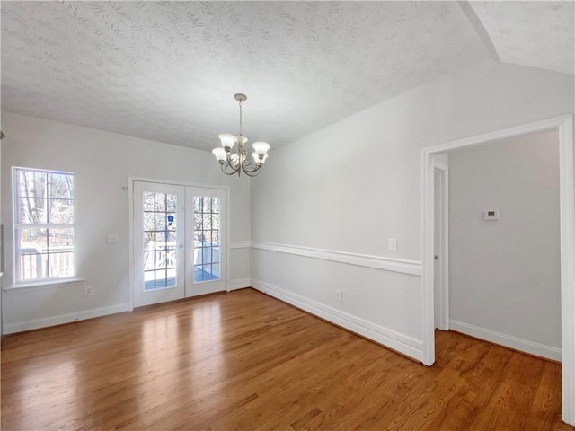 unfurnished room featuring french doors, a textured ceiling, an inviting chandelier, and light wood finished floors