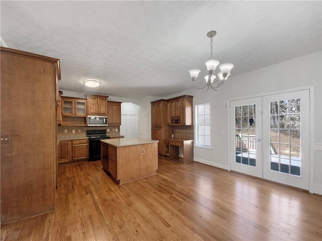 kitchen with stainless steel microwave, a center island, brown cabinetry, decorative backsplash, and black range oven