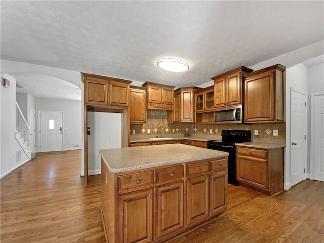 kitchen featuring stainless steel microwave, black range with electric stovetop, light wood-type flooring, brown cabinetry, and a sink