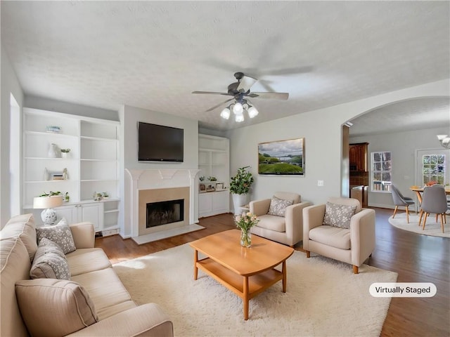 living area with arched walkways, a fireplace with flush hearth, a textured ceiling, and wood finished floors