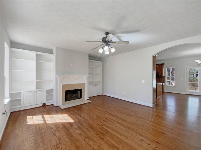 unfurnished living room with arched walkways, a textured ceiling, wood finished floors, and a premium fireplace