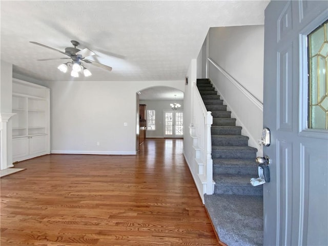 foyer with wood finished floors, baseboards, arched walkways, a textured ceiling, and ceiling fan with notable chandelier