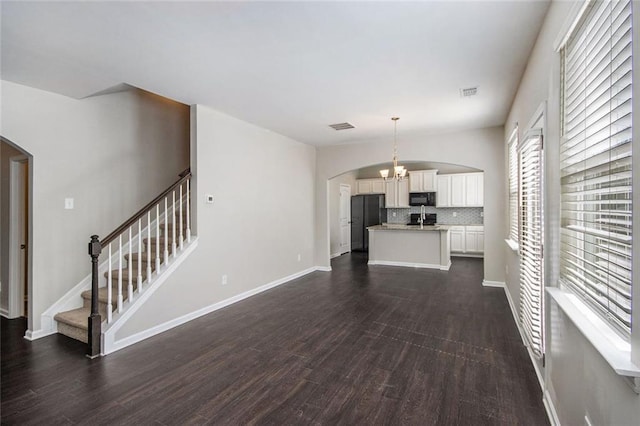 unfurnished living room with visible vents, dark wood finished floors, stairway, an inviting chandelier, and arched walkways