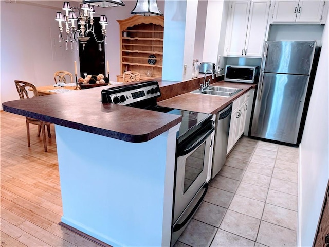 kitchen featuring kitchen peninsula, stainless steel appliances, sink, decorative light fixtures, and white cabinets