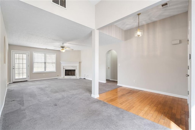 unfurnished living room with ceiling fan, a fireplace, visible vents, and arched walkways