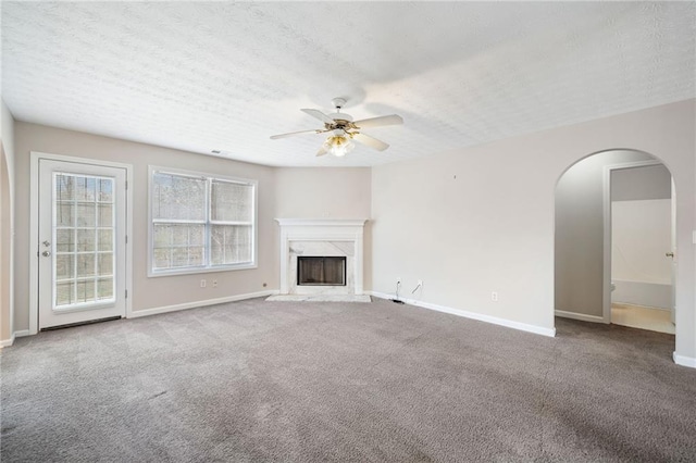 unfurnished living room featuring a textured ceiling, arched walkways, a fireplace, carpet flooring, and a ceiling fan