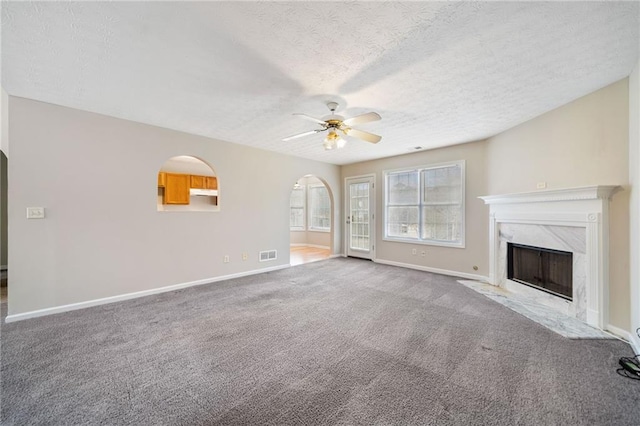 unfurnished living room with arched walkways, ceiling fan, carpet flooring, a high end fireplace, and visible vents