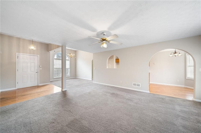 unfurnished living room featuring visible vents, arched walkways, a textured ceiling, carpet floors, and ceiling fan with notable chandelier