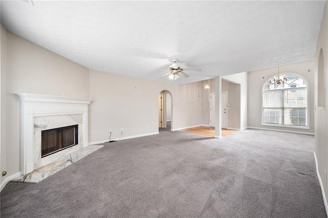 unfurnished living room featuring baseboards, arched walkways, ceiling fan, carpet flooring, and a high end fireplace