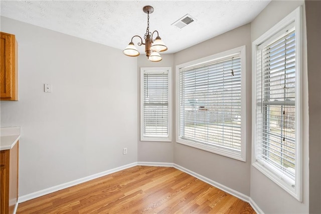 unfurnished dining area with baseboards, visible vents, light wood-style flooring, a textured ceiling, and a notable chandelier