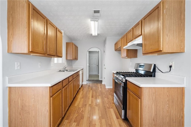 kitchen with arched walkways, stainless steel range with gas cooktop, visible vents, a sink, and under cabinet range hood