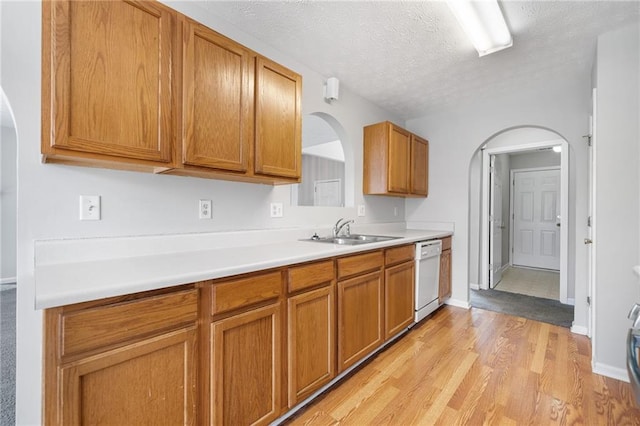 kitchen with brown cabinets, light wood finished floors, light countertops, white dishwasher, and a sink