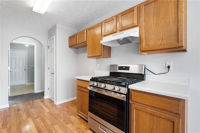 kitchen featuring arched walkways, light countertops, stainless steel range with gas stovetop, and under cabinet range hood