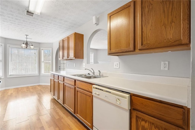 kitchen with brown cabinets, visible vents, light wood-style floors, white dishwasher, and a sink