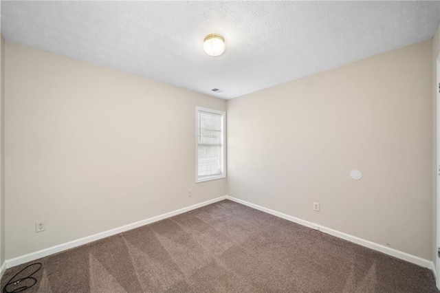 spare room with visible vents, dark carpet, a textured ceiling, and baseboards