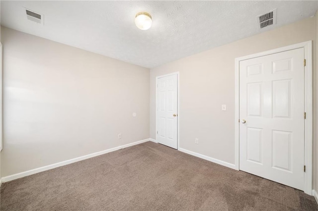 spare room featuring a textured ceiling, carpet floors, visible vents, and baseboards