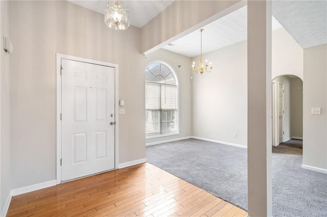 entrance foyer with baseboards, arched walkways, wood finished floors, carpet floors, and a chandelier