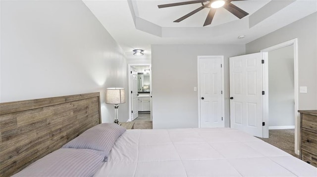 carpeted bedroom with a tray ceiling, a ceiling fan, baseboards, and ensuite bathroom