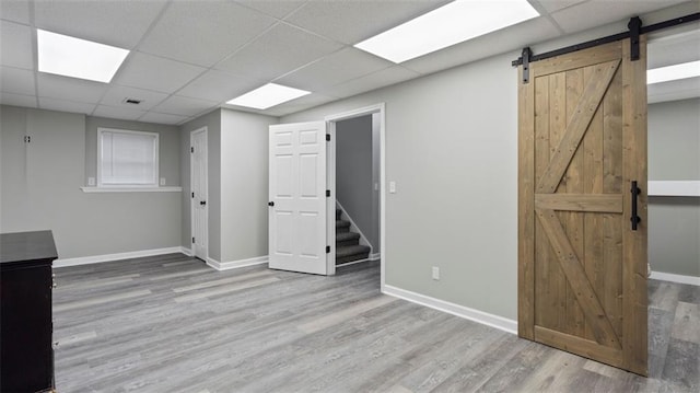 below grade area with wood finished floors, visible vents, baseboards, a paneled ceiling, and a barn door