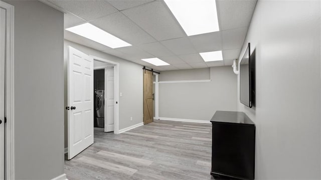 interior space with a barn door, a drop ceiling, light wood finished floors, and washer / dryer