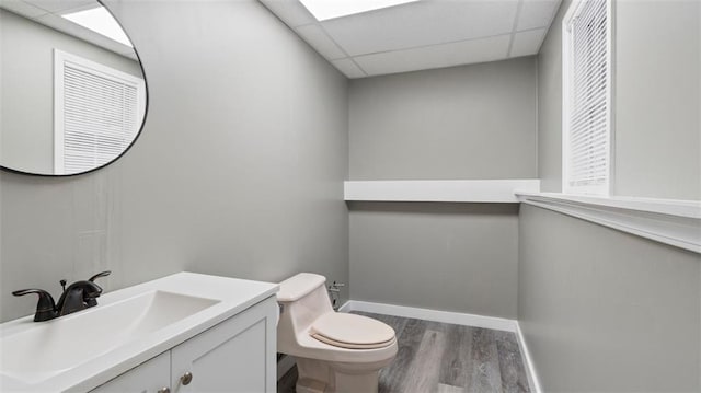 bathroom featuring toilet, wood finished floors, a paneled ceiling, baseboards, and vanity