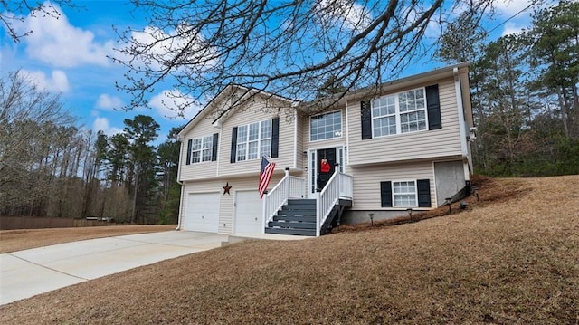 raised ranch with a front lawn, an attached garage, and driveway