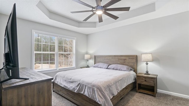 carpeted bedroom featuring a tray ceiling, baseboards, and ceiling fan