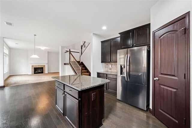 kitchen with stainless steel refrigerator with ice dispenser, decorative backsplash, light stone counters, a kitchen island, and dark hardwood / wood-style flooring