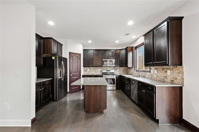 kitchen with light stone counters, dark hardwood / wood-style flooring, a kitchen island, and stainless steel appliances