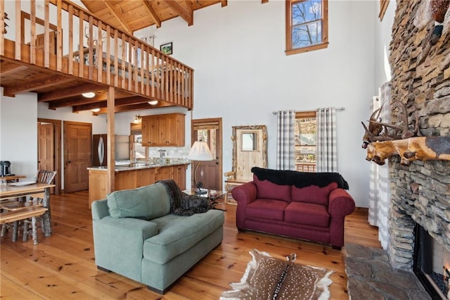 living area with light wood-type flooring, wood ceiling, beam ceiling, and a stone fireplace