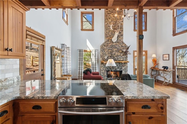 kitchen with light stone counters, light wood finished floors, stainless steel electric stove, decorative backsplash, and a stone fireplace