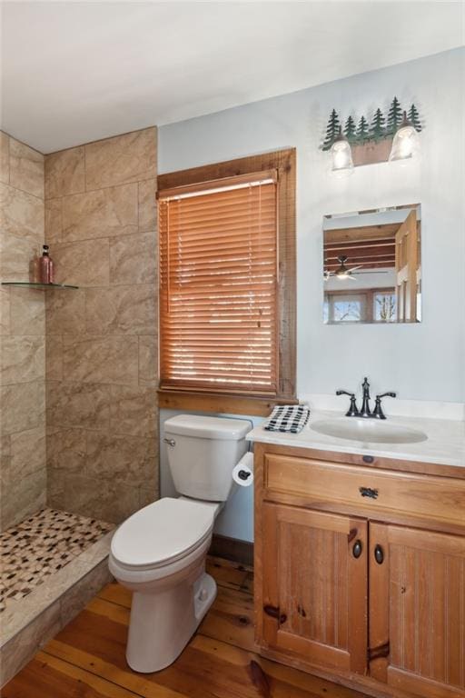 bathroom with toilet, vanity, tiled shower, and wood finished floors