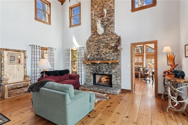 living area with baseboards, a fireplace, a towering ceiling, and hardwood / wood-style floors